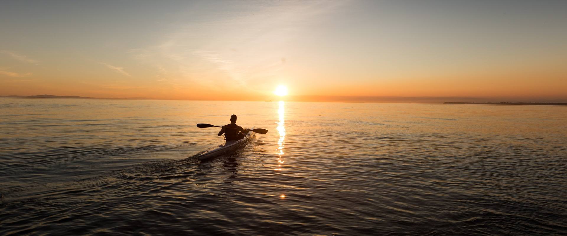 Persona in kayak che si dirige verso l'orizzonte con splendido tramonto